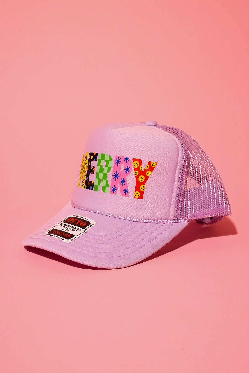 Side view of a lavender trucker hat with the text 'MERRY' in different patterns on a pink background