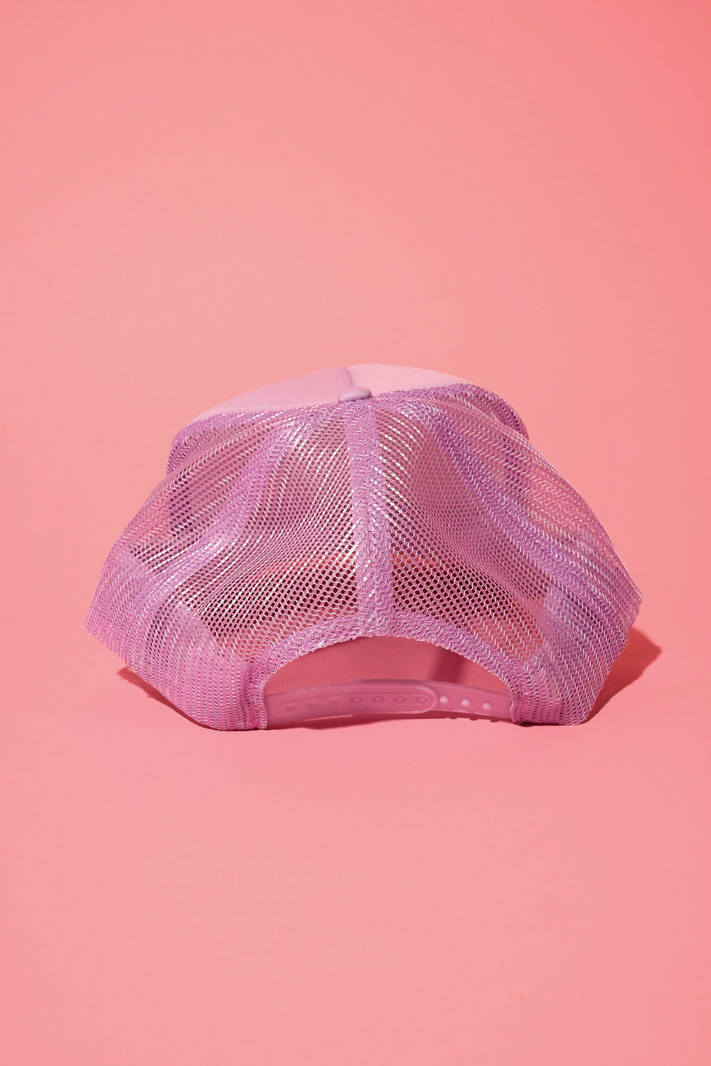Back view of a lavender trucker hat on a pink background