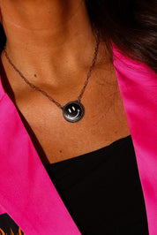 Model wearing a bright pink blazer and silver necklace with a black smiley face charm