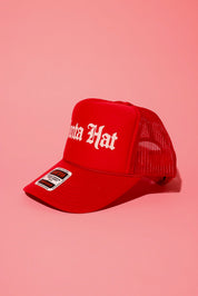 Side view of a red trucker hat with white text that reads 'Santa Hat' on a pink background