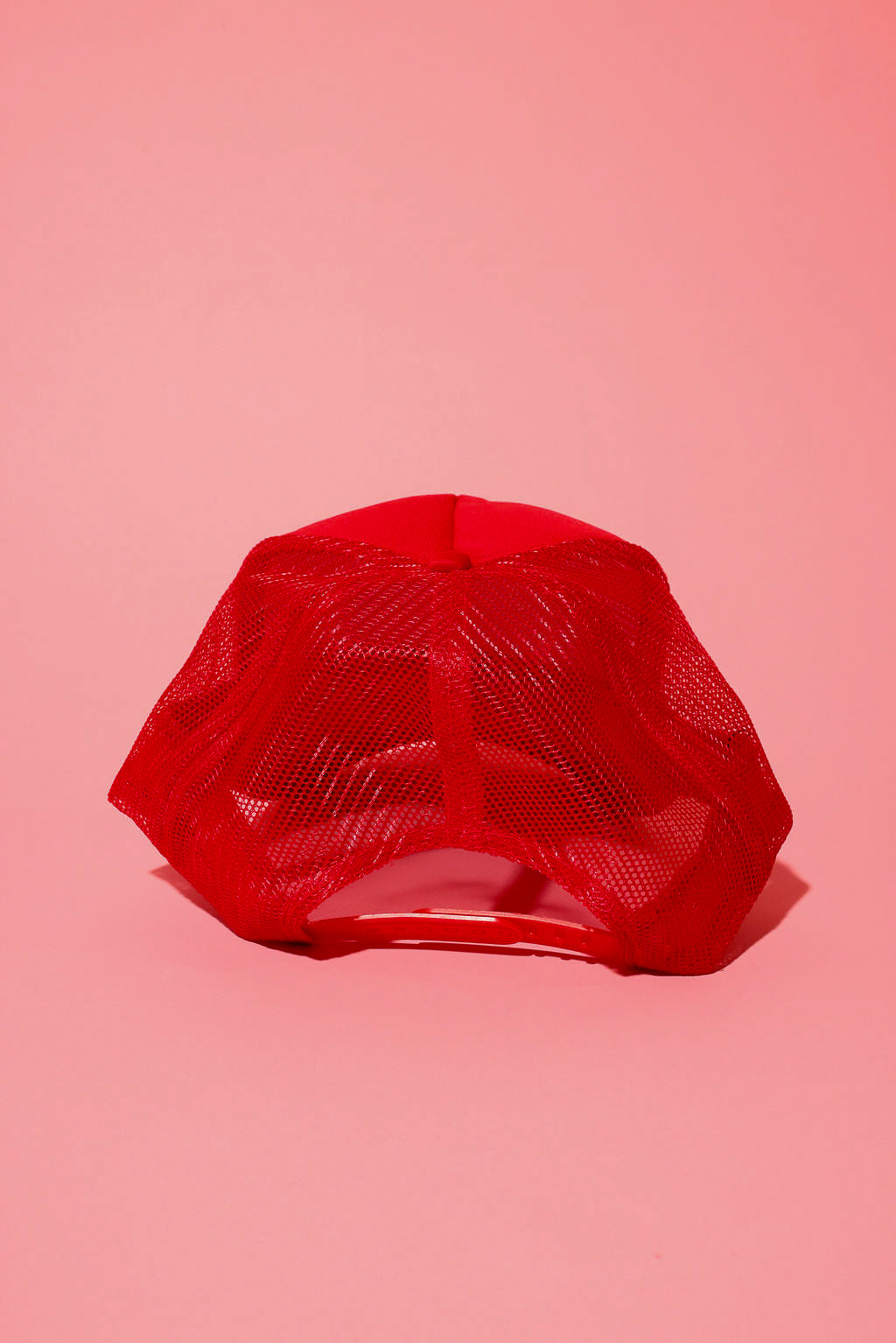 Back view of a red trucker hat on a pink background