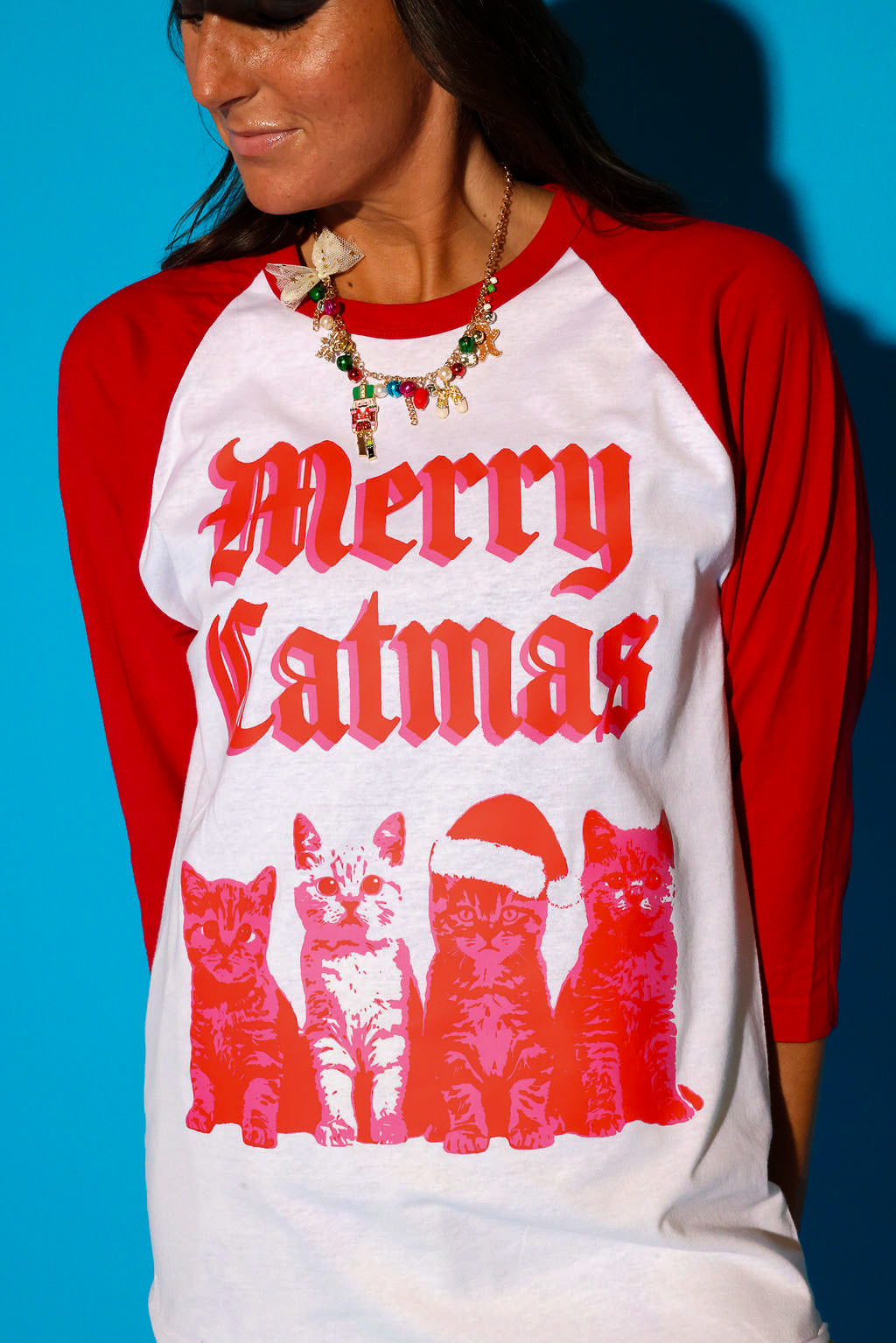A model wearing a baseball tee with a red graphic and a holiday necklace with colorful beads and a nutcracker on a blue background