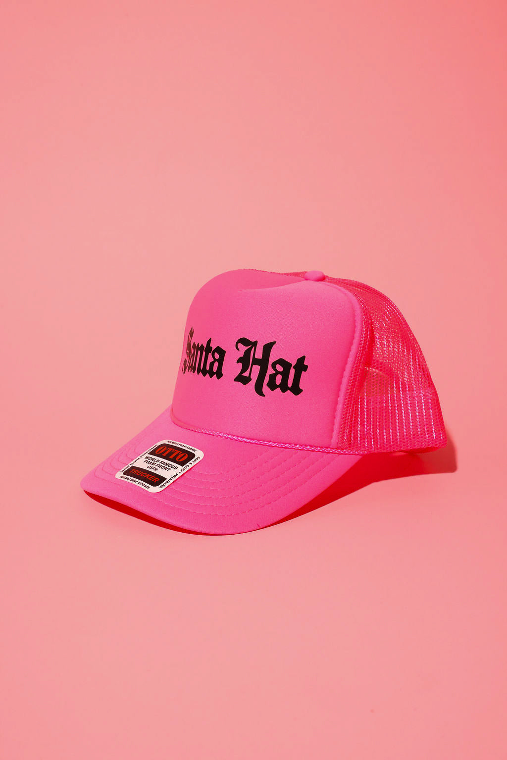 Side view of a neon pink trucker hat with black text that reads 'Santa Hat' on a pink background