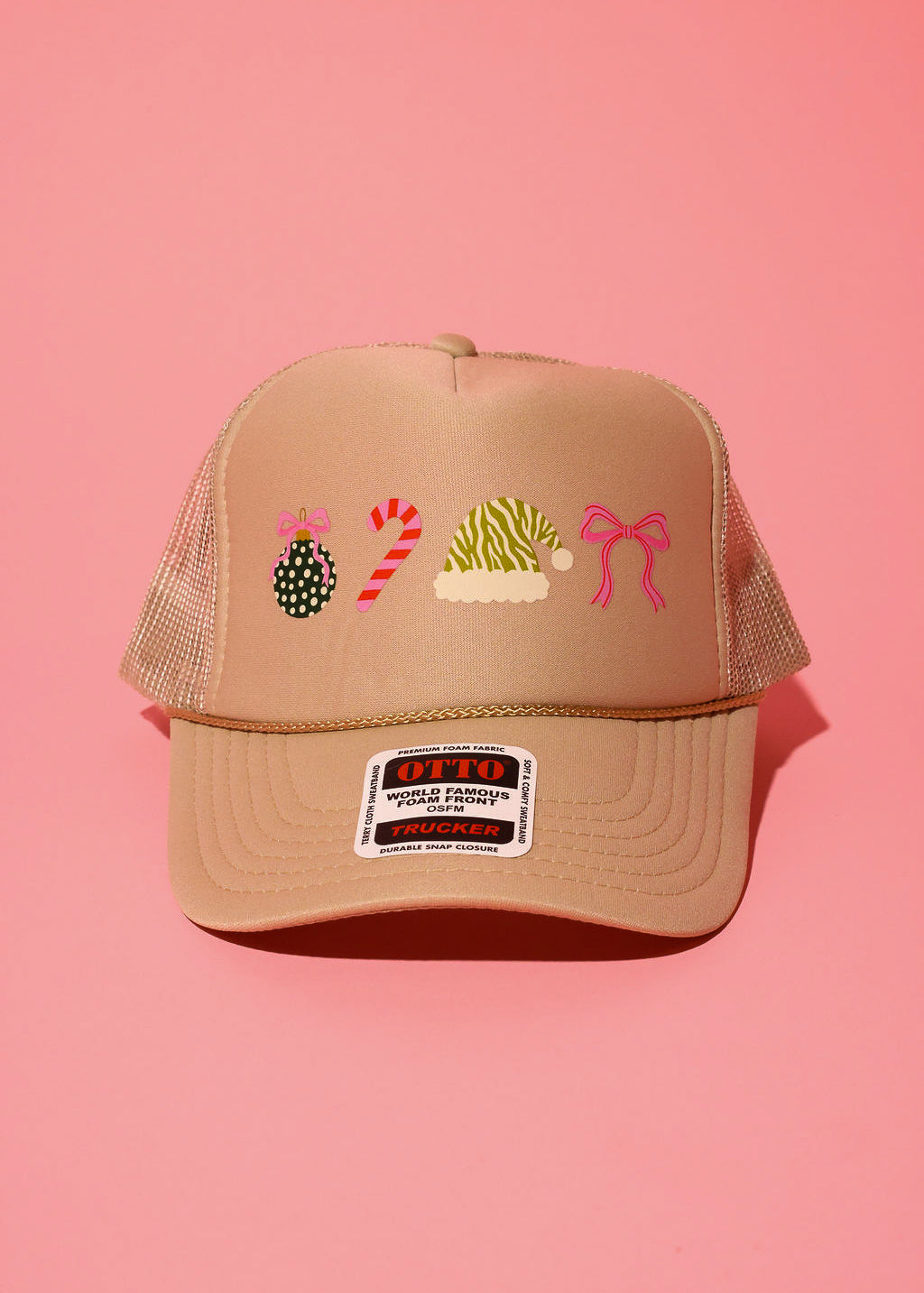 Khaki trucker hat with different graphics such as an ornament, candy cane, Santa hat, and bow on a pink background