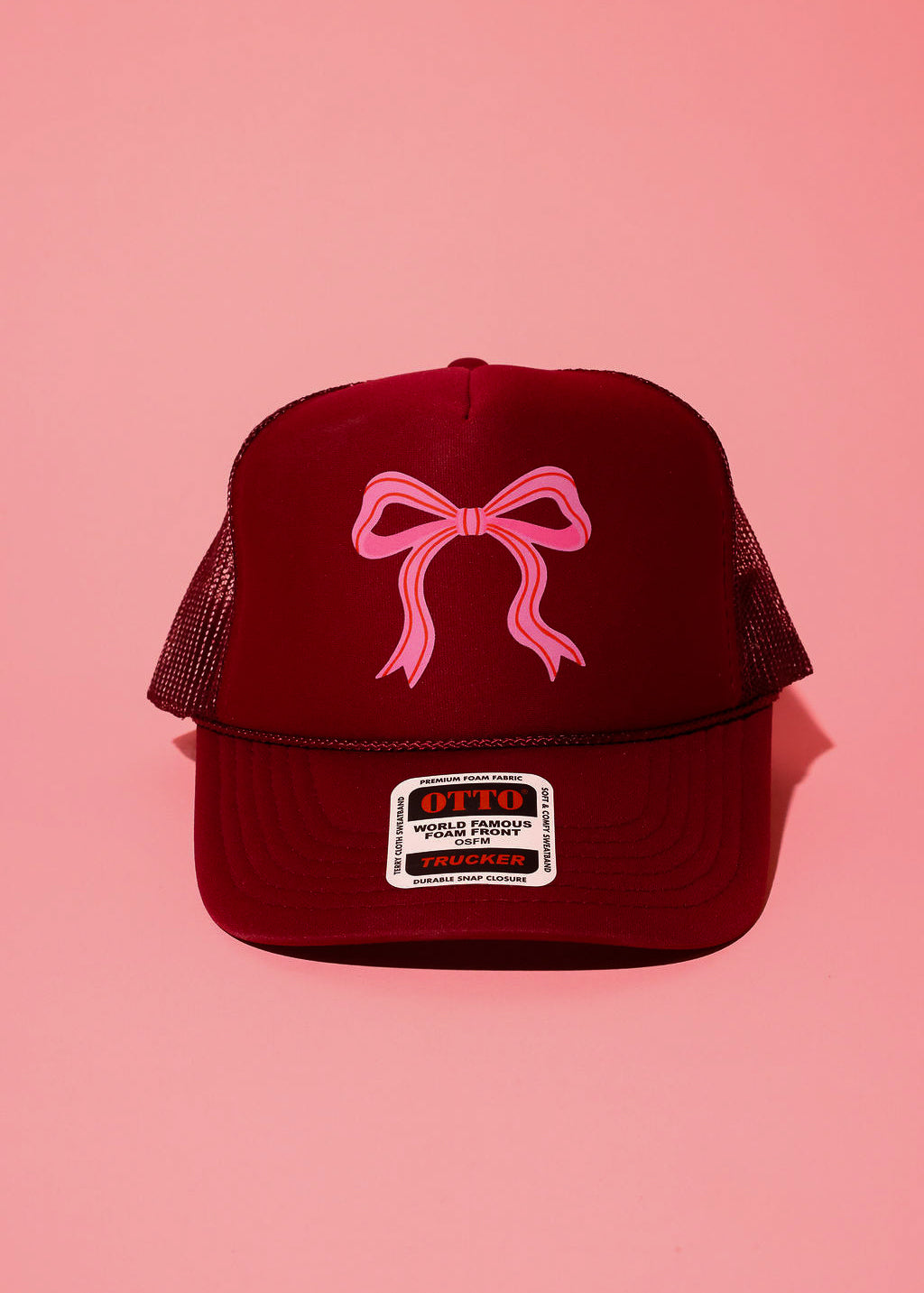 Maroon trucker hat with a pink bow on a pink background