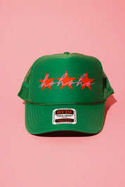 A green trucker hat with three red stars and cursive text in pink that reads 'ho ho ho' on a pink background