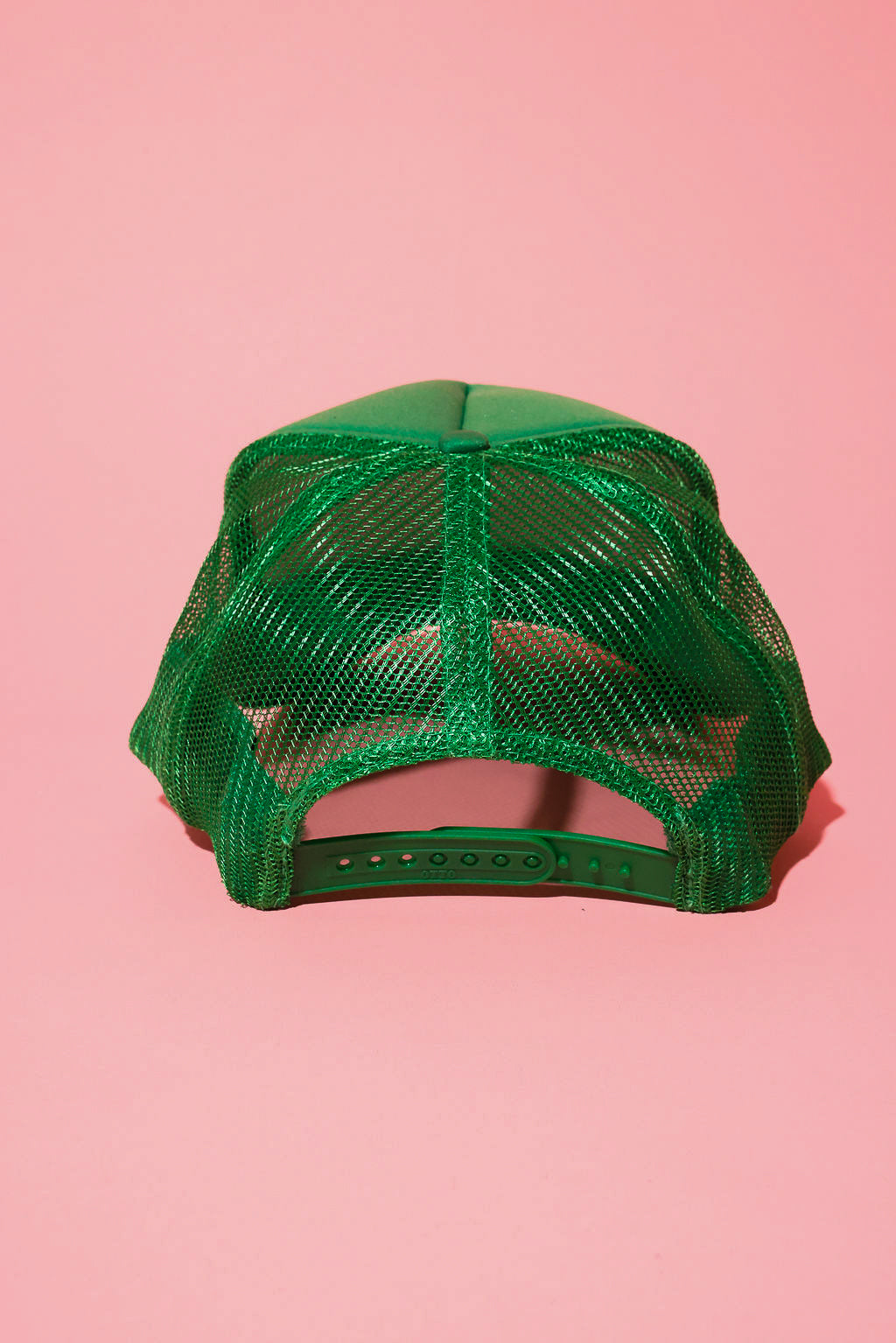 Back view of a green mesh trucker hat on a pink background