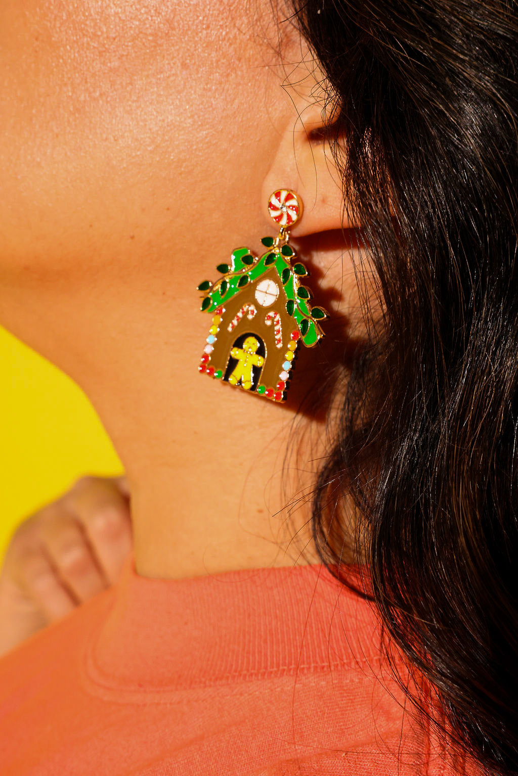 Close up side view of a model wearing an orange tee and gingerbread earrings on a yellow background