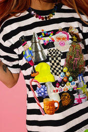 Model wearing a black and white striped tee with a Christmas graphic and a rainbow jeweled necklace on a pink background