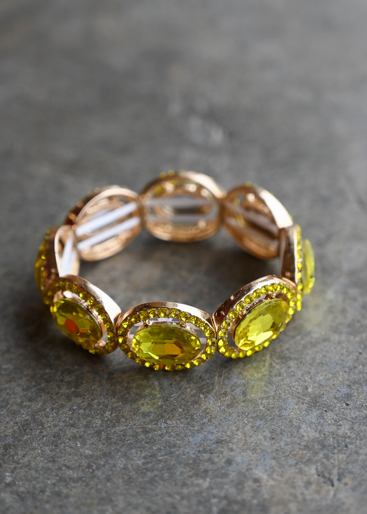A rose gold eternity-style band ring featuring large oval yellow gemstones surrounded by small clear stones, photographed on a textured gray surface