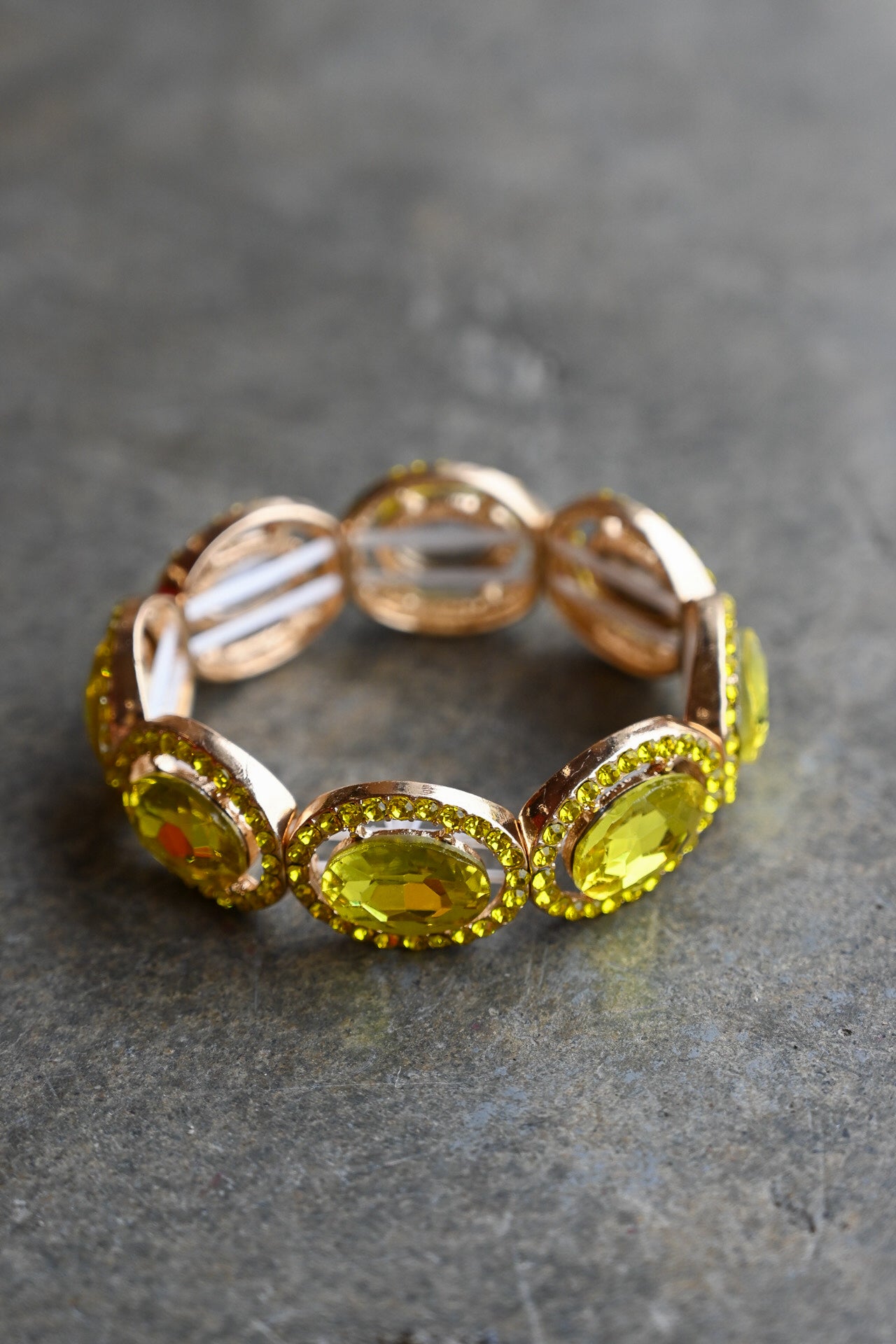 A rose gold eternity-style band ring featuring large oval yellow gemstones surrounded by small clear stones, photographed on a textured gray surface
