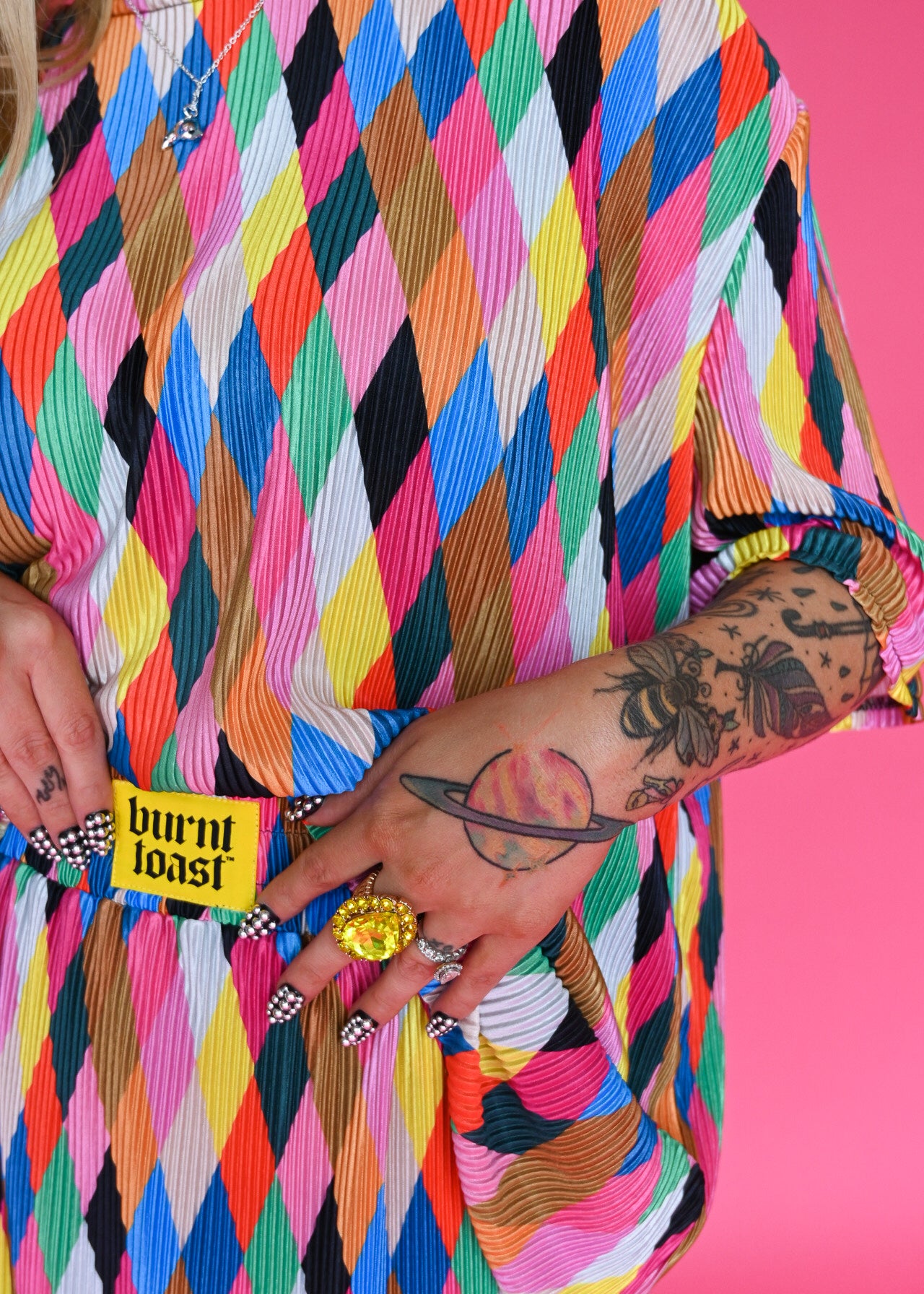 diamond pattern in pink, blue, yellow, orange, black, and white. The waistband has a yellow patch that reads 'burnt toast' against a solid pink background