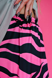 A close-up of a person wearing bright pink and black wavy striped pants, with a gray top and a vivid pink background visible