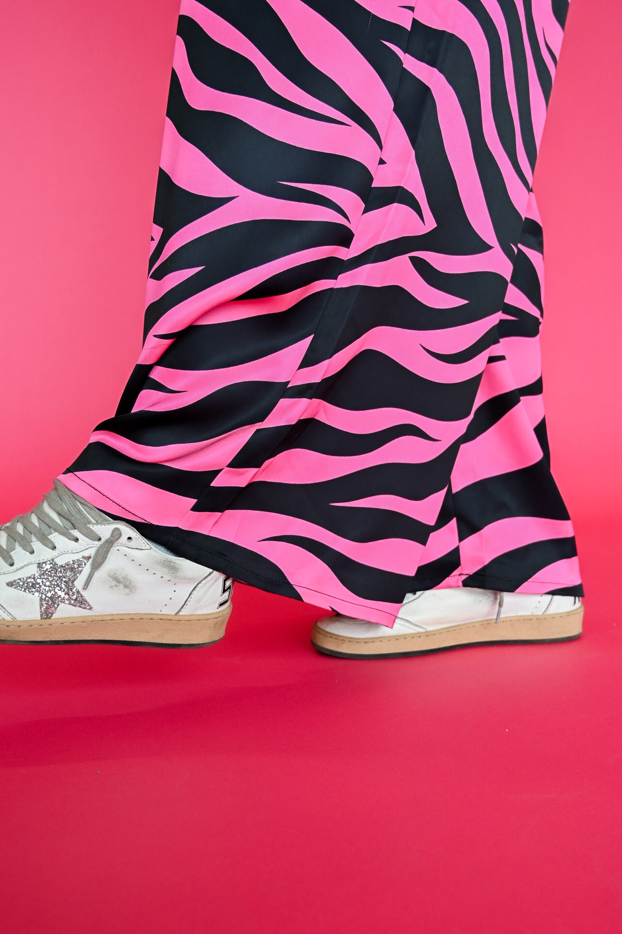 Pink and black zebra-print pants worn with white sneakers, shown from the knees down against a solid pink background
