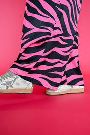 Pink and black zebra-print pants worn with white sneakers, shown from the knees down against a solid pink background