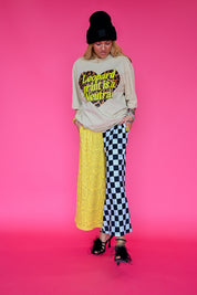 A model wearing a beige graphic tee that says 'leopard print is a neutral' and half and half pants that are yellow snakeskin, and black & white checkered patterned, on a pink background