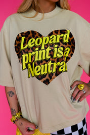 A person wearing an oversized cream-colored t-shirt with a large leopard-print heart graphic and the text 'Leopard print is a Neutra' in yellow. The background is a solid bright pink