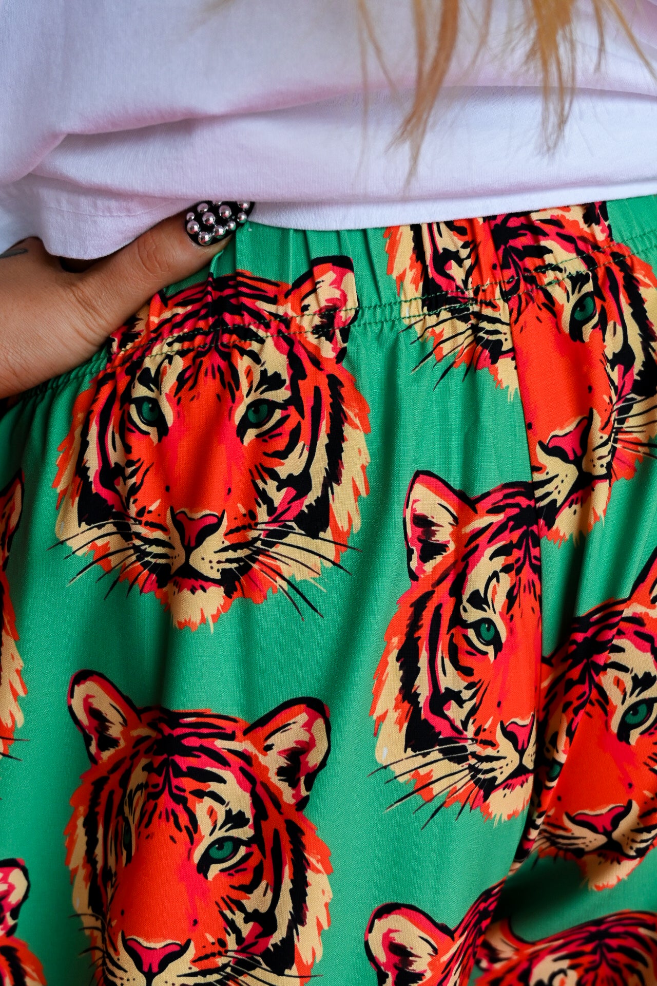 Close-up of a person wearing bright green pants with a bold orange, red, and black tiger face print, paired with a white top