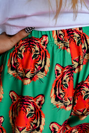 Close-up of a person wearing bright green pants with a bold orange, red, and black tiger face print, paired with a white top