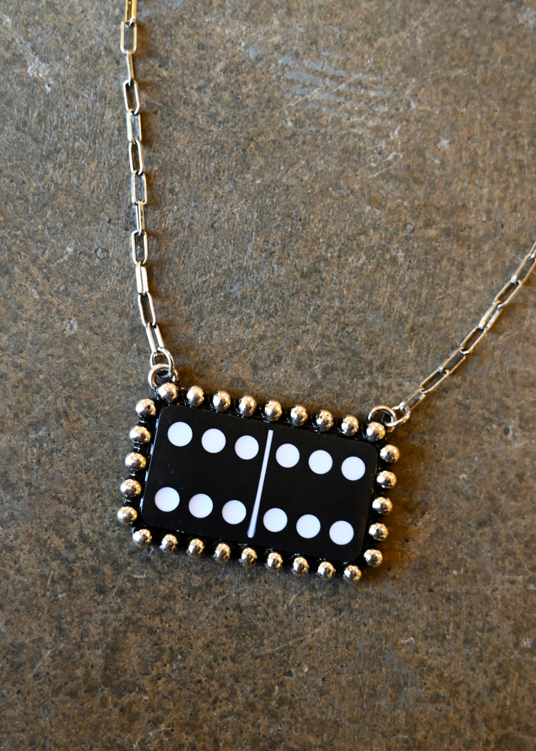Close up of a silver chain necklace with a black and white domino pendant on a dark background