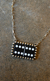 Close up of a silver chain necklace with a black and white domino pendant on a dark background
