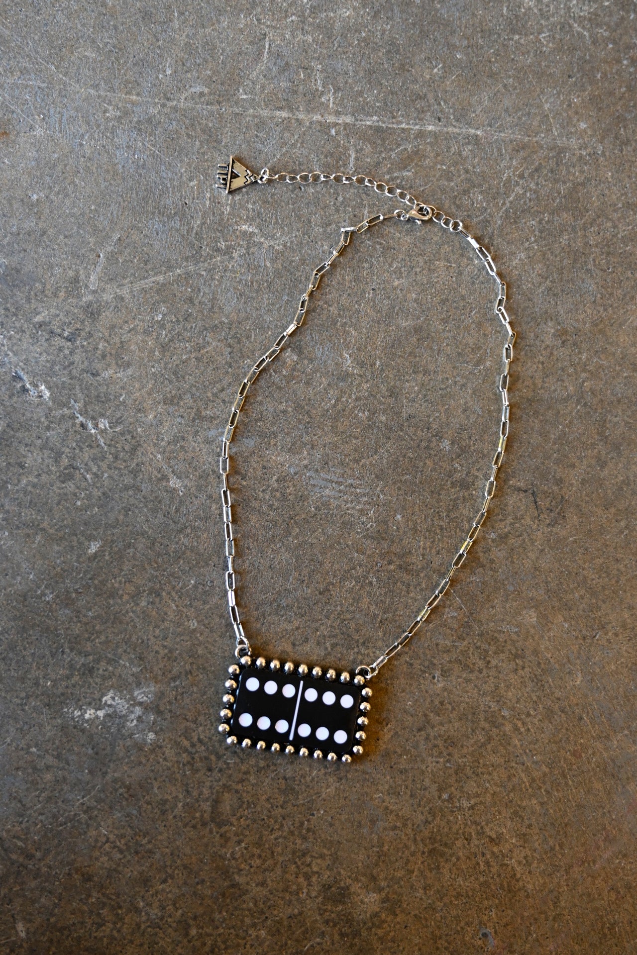 A silver chain necklace with a black and white domino pendant on a dark background