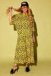 Model wearing a black and yellow leopard set black high heels and a black trucker hat that says 'mother' on it, against a pale yellow background