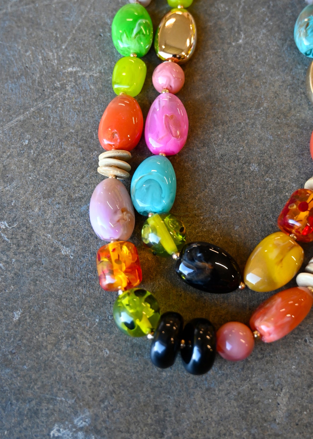 Close up of a gold chain necklace with multicolored beads in various shapes on a dark background