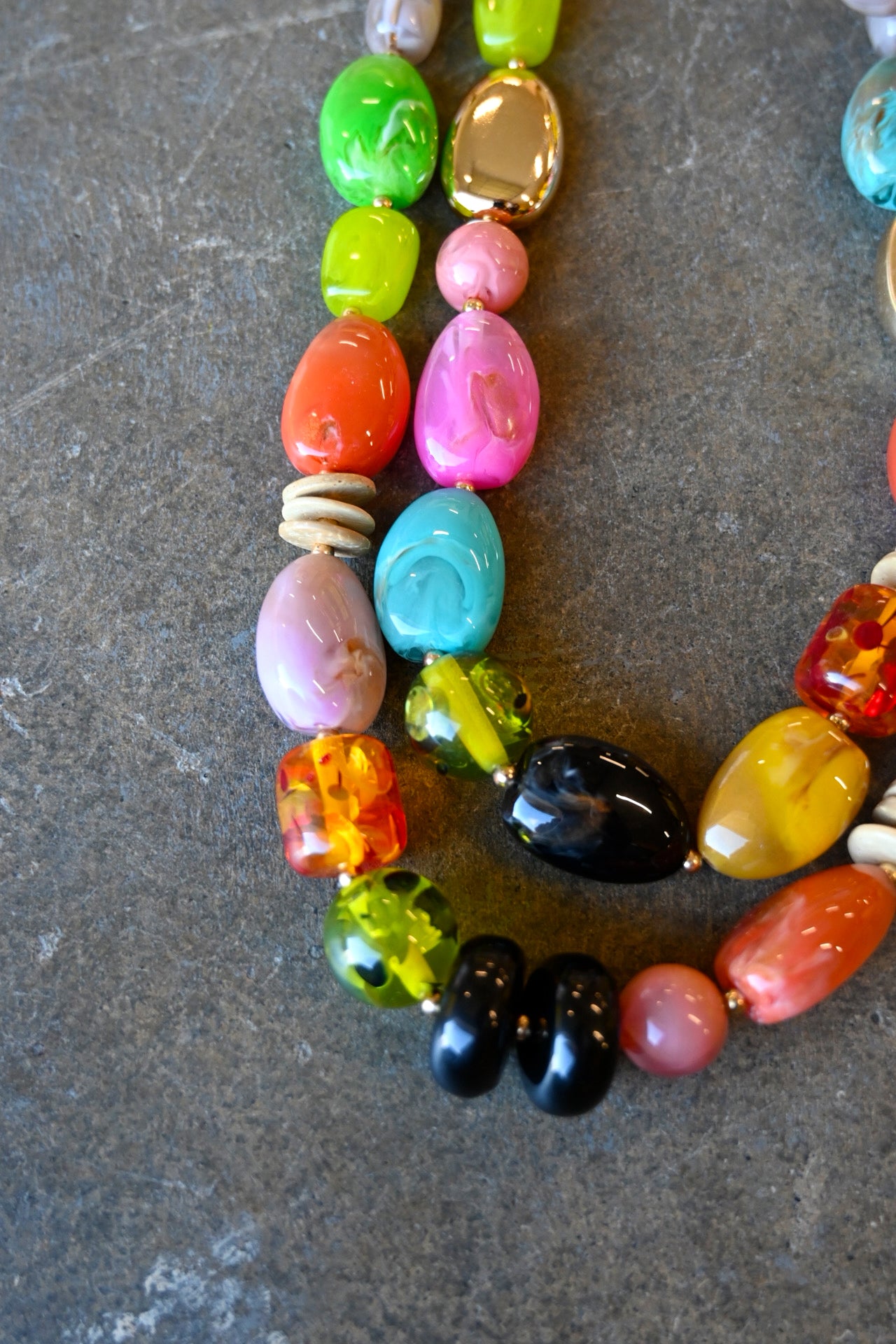 Close up of a gold chain necklace with multicolored beads in various shapes on a dark background