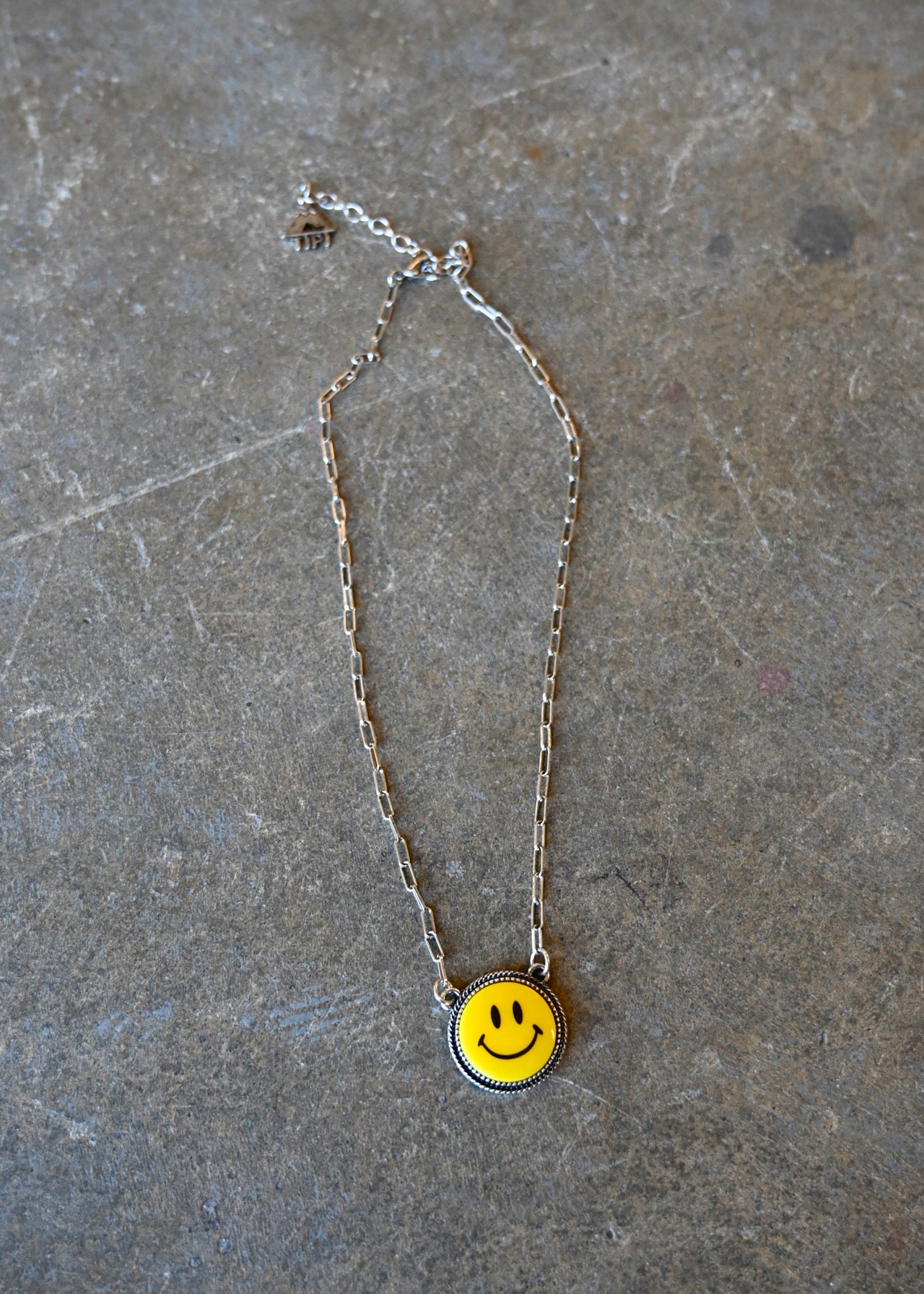 A silver chain necklace with a yellow smiley pendant on a dark background