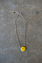 A silver chain necklace with a yellow smiley pendant on a dark background