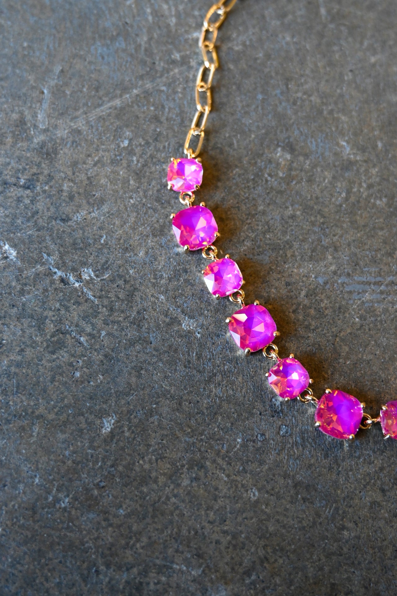 Close up of a  gold chain necklace with square neon pink gems on a dark background
