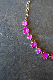 Close up of a  gold chain necklace with square neon pink gems on a dark background