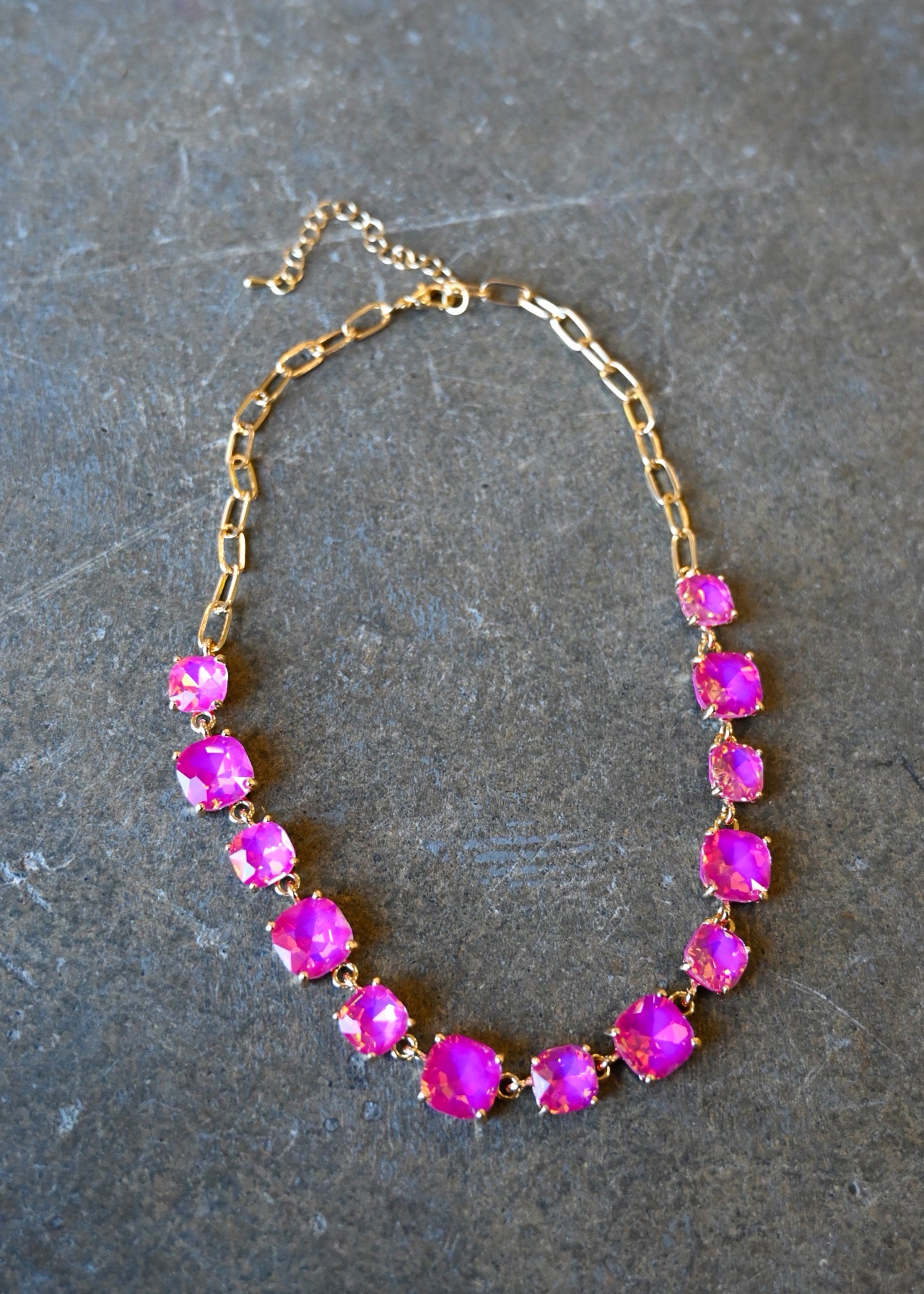 A gold chain necklace with square neon pink gems on a dark background