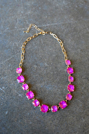 A gold chain necklace with square neon pink gems on a dark background