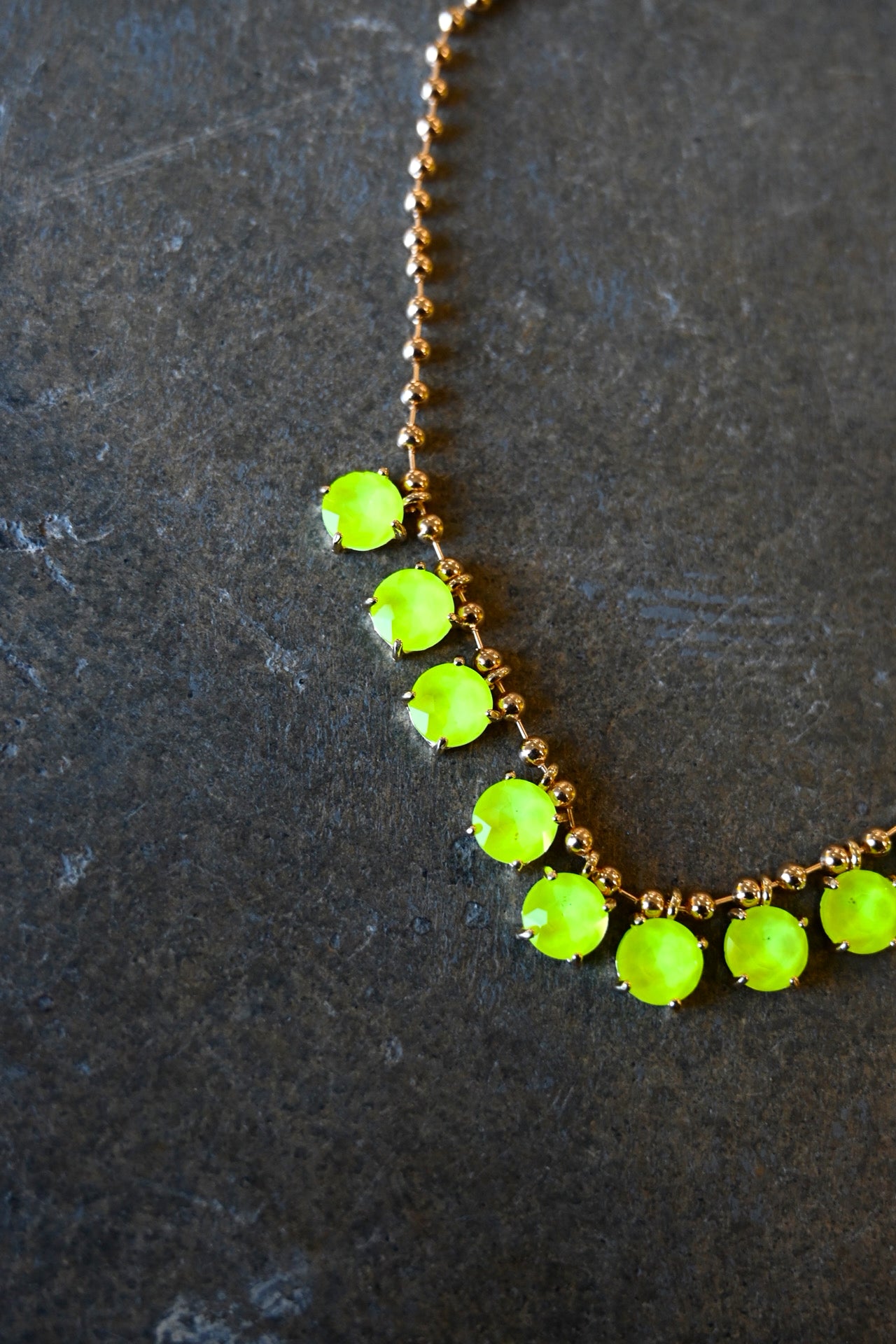 Close up of a gold chain necklace with neon yellow gems on a dark background