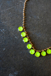 Close up of a gold chain necklace with neon yellow gems on a dark background