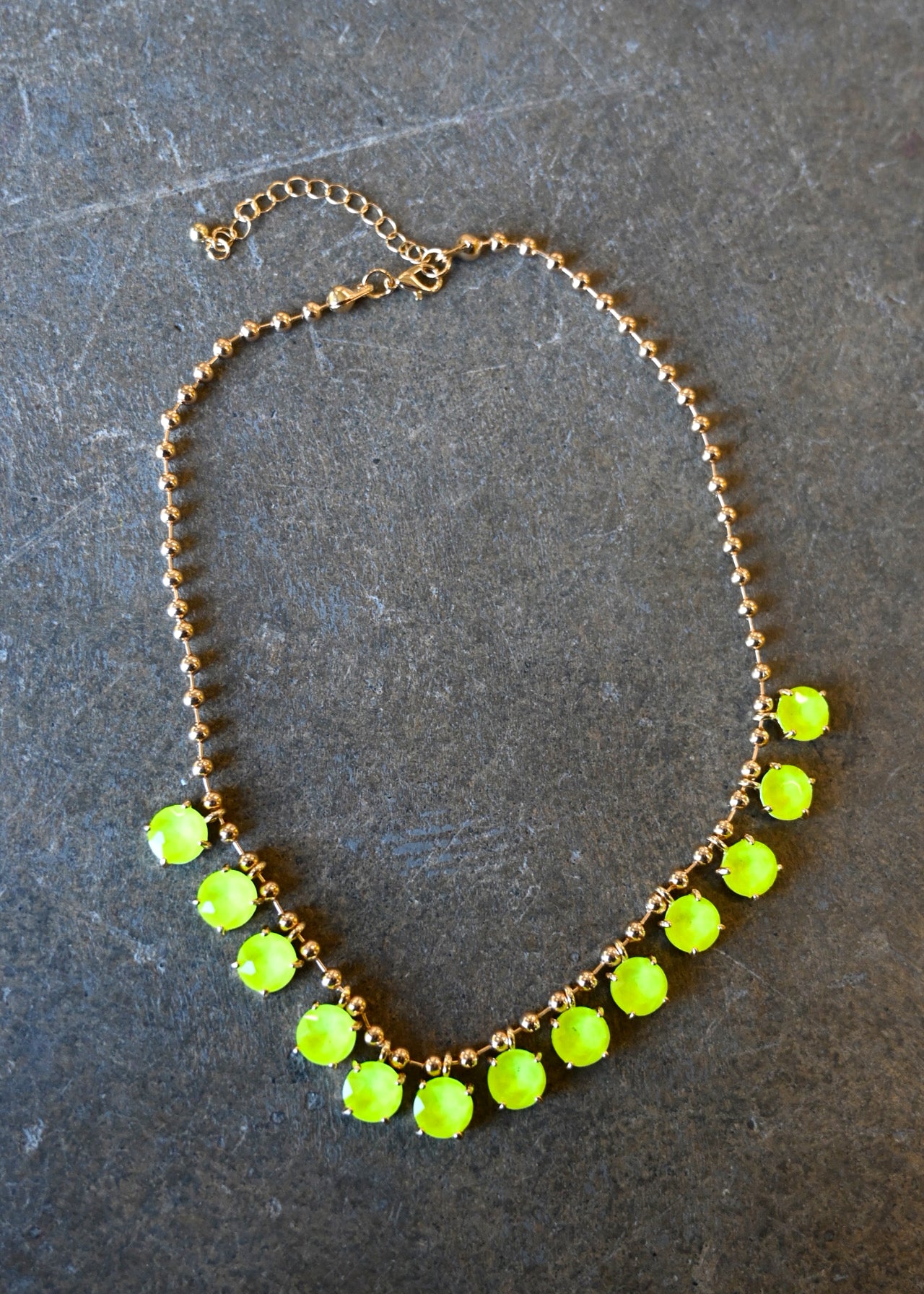 A gold chain necklace with neon yellow gems on a dark background
