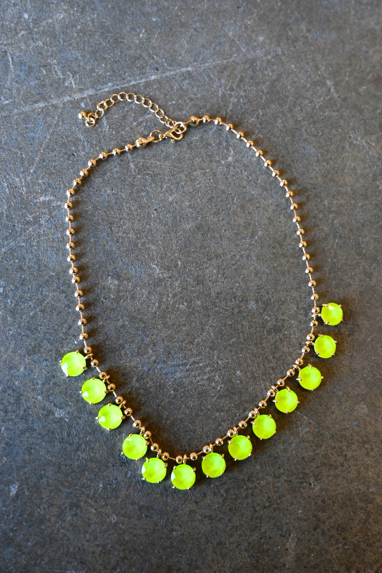A gold chain necklace with neon yellow gems on a dark background