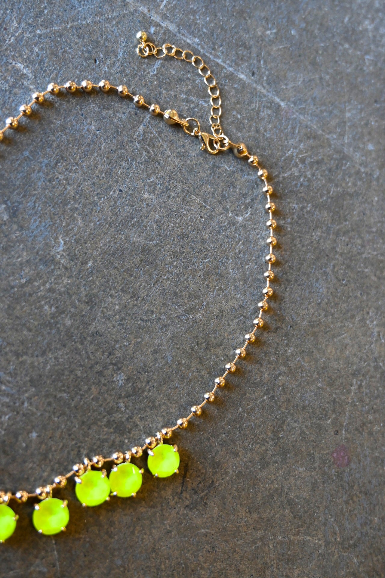 Close up of a gold chain necklace with neon yellow gems and a clasp on a dark background