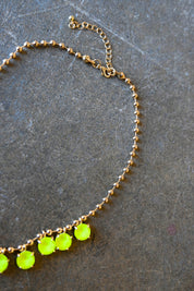 Close up of a gold chain necklace with neon yellow gems and a clasp on a dark background
