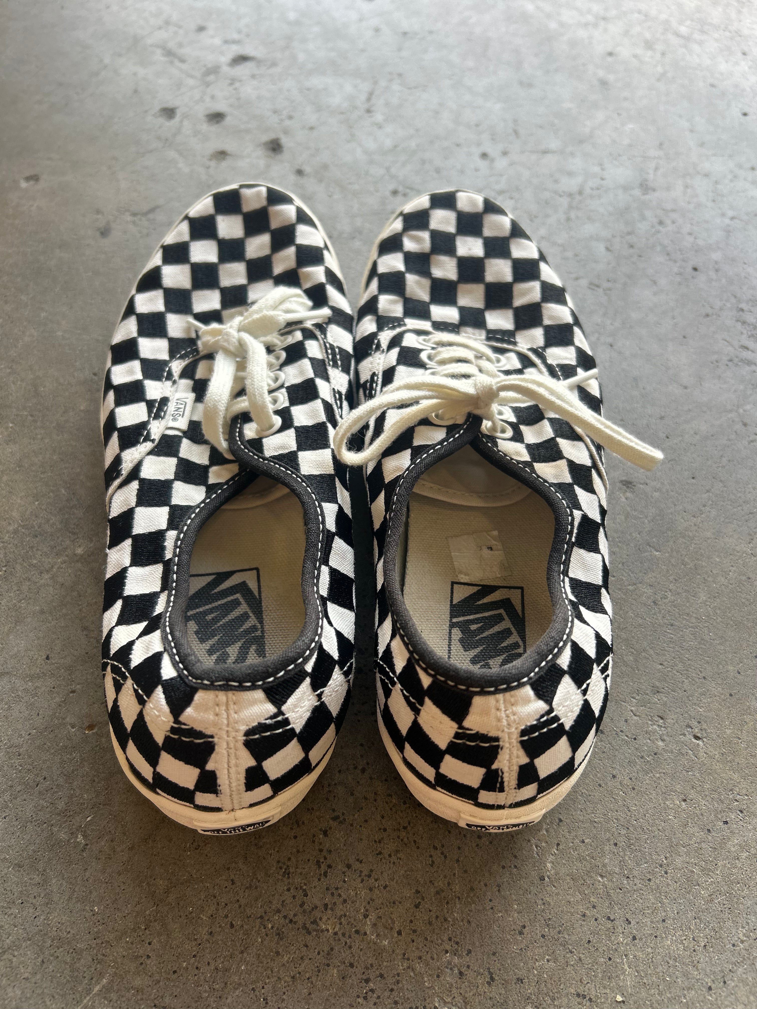 A pair of Vans checkerboard canvas low-top sneakers with off-white laces, shown from a top-down view on a gray concrete floor
