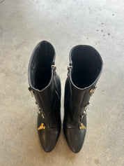 A pair of black leather ankle boots with gold-tone hardware and decorative details, photographed from above on a gray concrete floor