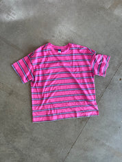 A pink short-sleeve t-shirt with horizontal navy and purple stripes, laid flat on a gray concrete floor
