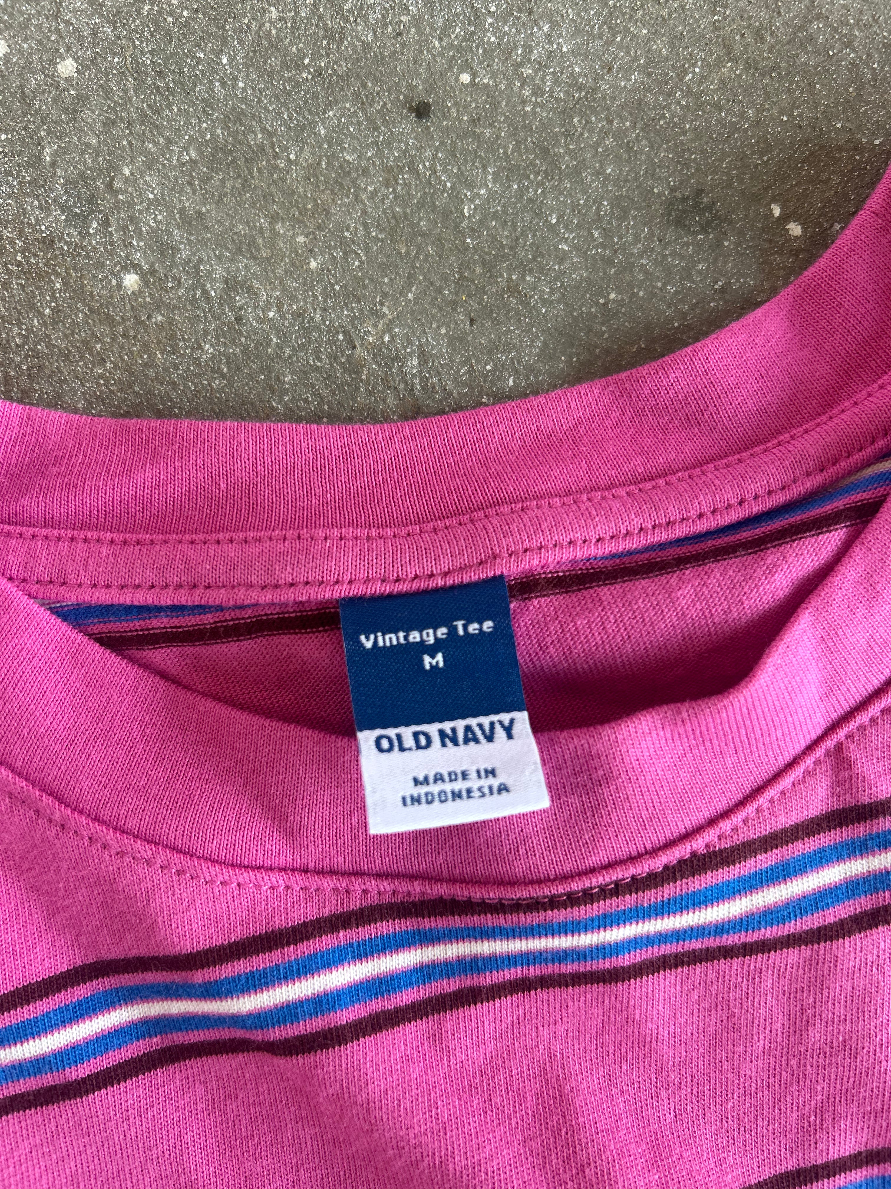 Close-up of a pink striped t-shirt collar showing the blue and white 'OLD NAVY' vintage size M tag, laid flat on a gray concrete surface
