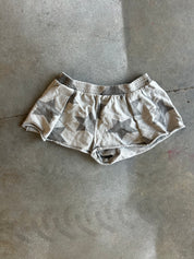A pair of low-rise shorts with a gray and beige star camouflage pattern, laid flat on a concrete floor