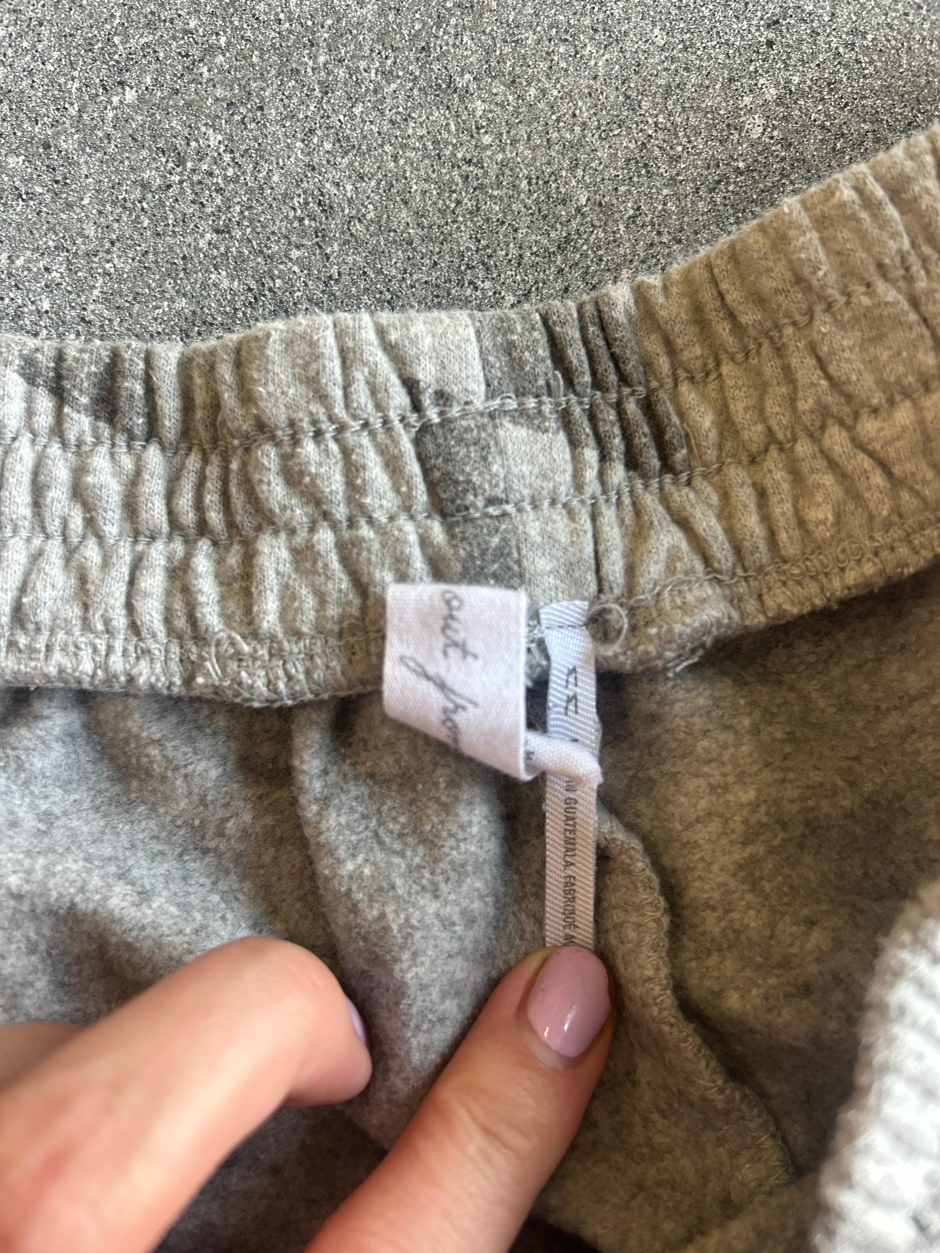 Close-up of the waistband and inner label of a pair of gray jogger sweatpants, with a person's fingers pointing to the white fabric brand tag