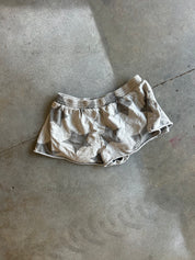 A pair of short, loose-fitting shorts with an abstract gray and beige star-like pattern, laid flat on a concrete floor