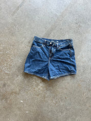 A pair of vintage blue denim shorts with a frayed hem, laid flat on a textured concrete floor