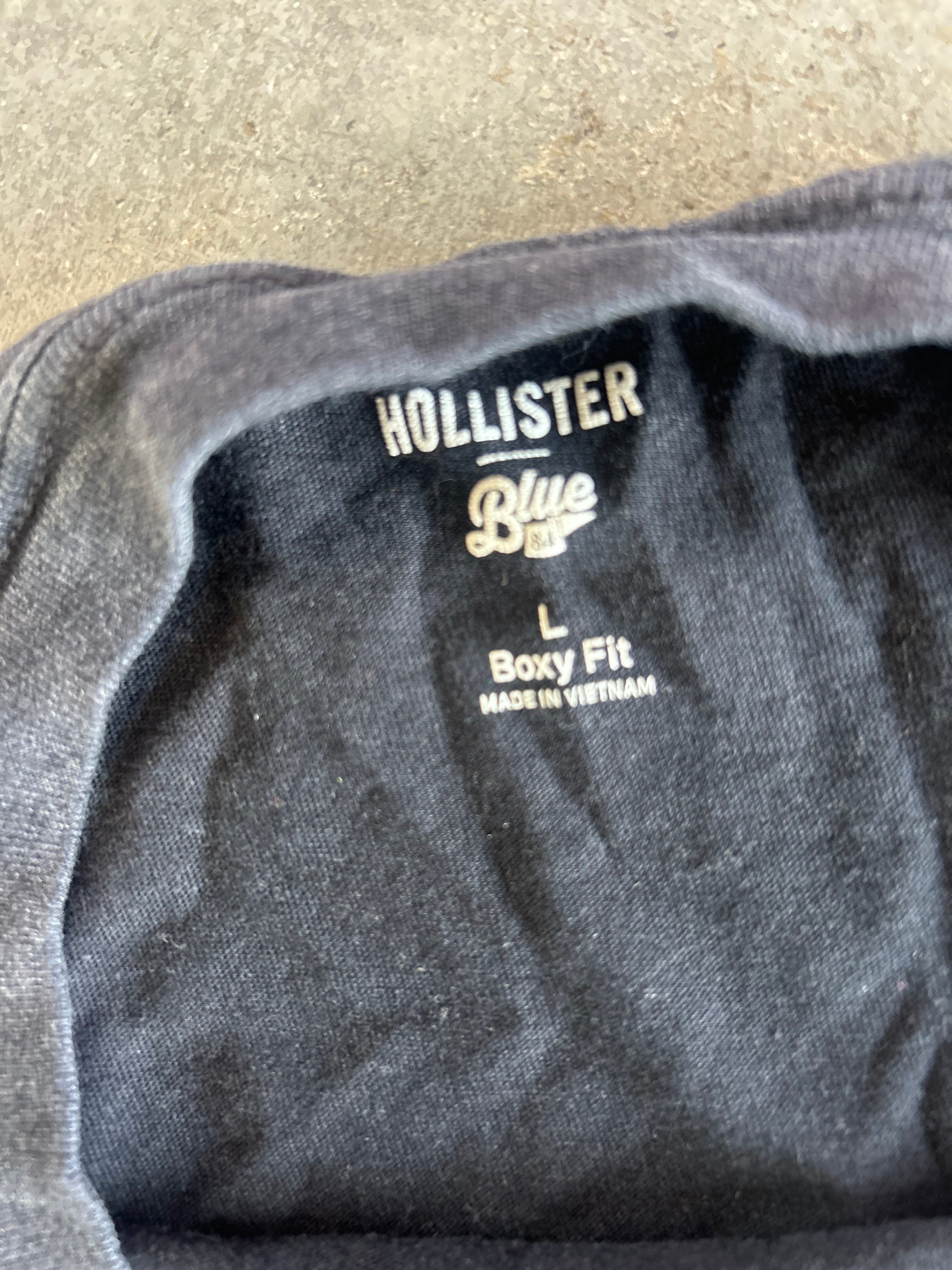 Close-up of the inside collar of a dark gray Hollister t-shirt, showing the brand's 'Blue Label' label with 'Hollister', 'Blue Label', 'L', and 'Boxy Fit' printed in white